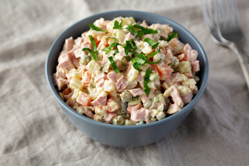 Homemade Olivier salad in a Bowl on a white wooden background, side view.