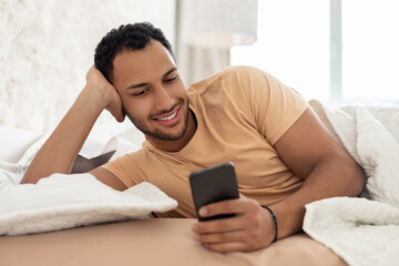 Middle Eastern Guy Using Cellphone And Mobile Application In Bedroom