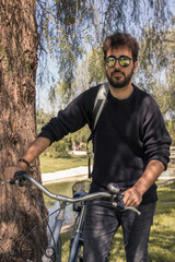 Obraz premium Young man with curly hair wearing sunglasses and backpack enjoying a sunny day with his bike.