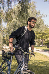 Young man with curly hair wearing sunglasses and backpack enjoying a sunny day with his bike.