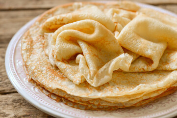 Pancakes (bliny) in a plate on a wooden background.