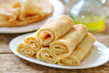Thin pancakes (bliny). Pancakes rolled into tubes on a white plate. Wooden background.