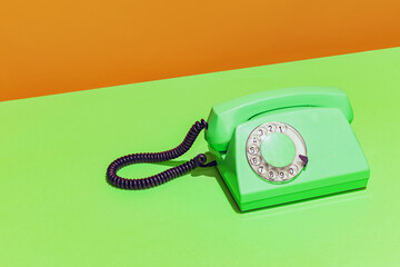 Colorful bright image of green neon retro telephone on light green and orange background