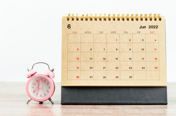 Naklejka premium June 2022 Desk calendar with pink alarm clock on wooden table.