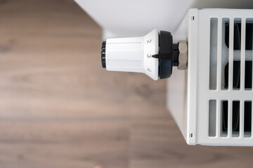 The white thermostat for adjusting the central heating radiator is set to the medium economical mode of maintaining the temperature in the room