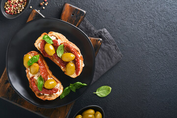 Bruschetta with sun dried tomatoes. Toast or sandwich with ricotta, sun dried tomatoes and Provence herbs with basil servered on black plate on black background table. Top view banner menu recipe.
