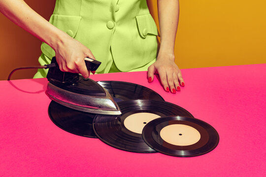 Colorful bright image of woman using retro iron and ironing vintage vinyl records isolated over pink background.