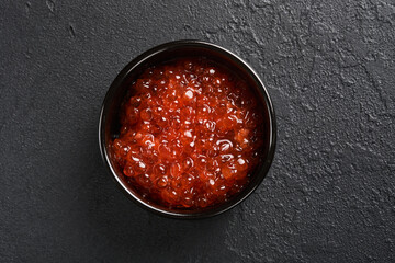 Red salmon caviar. Delicious red caviar in black bowl on black dark concrete background. Top view with copy space. Flat lay. Mock up.