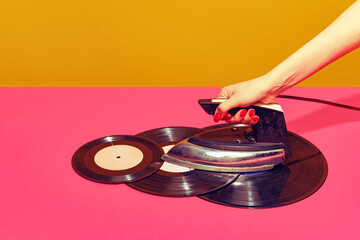 Colorful bright image of woman using retro iron and ironing vintage vinyl records isolated over pink background. Creativity