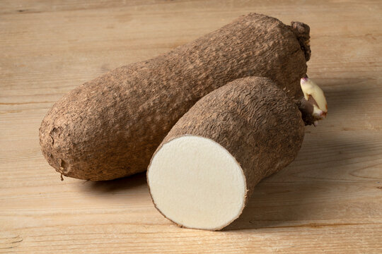  Whole and halved raw African yam on wooden background close up
