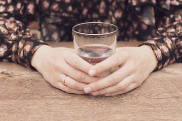 Young woman's hands holding a glass of pure water in morning after waking up. Young girl maintains water balance for body health by drinking transparent cup of clean water. Long web banner. High