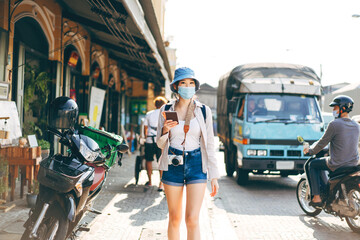 Portrait young adult asian woman backpack traveller wear face mask camera and blue hat at city outdoor