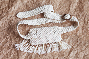 Handmade macrame belt bag on craft paper background. ECO friendly natural macrame cotton waist bag. Hobby knitting handmade macrame. Modern summer concept.