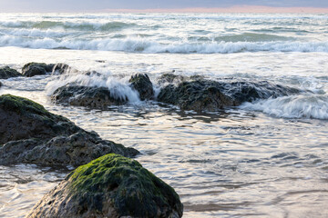 Beautiful waves with white foam crashing on the big rocks at the shore of Cap Blanc-Nez, France with a beautiful dramatic sunset in the background. High quality photo
