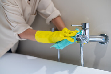 A service woman polishing faucet in the bathroom