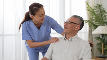 Closeup of caring Asian woman nursing aide talking and encouraging older male patient during home...