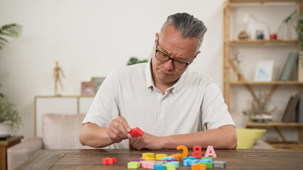 asian senior male with dementia trying to recognize and arrange color letter blocks in order at...