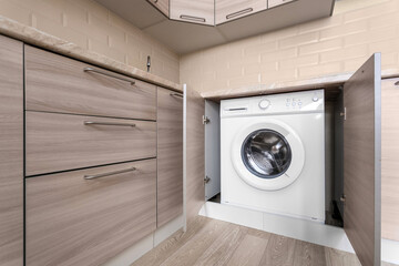 White washing machine built into a beige wooden kitchen cabinet