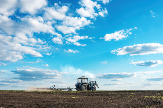 tractor plows the large soil field against blue cloudy sky background in spring season