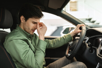 Unhappy young man sitting on driver's seat of new car, disappointed with test drive, having doubts...