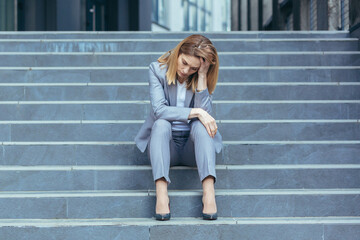Depressed sad woman sitting on the stairs of a business building, businesswoman in business clothes...