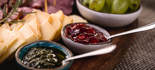 red fruit jam served with pesto sauce on a cheese board and salami, typical European winter snacks