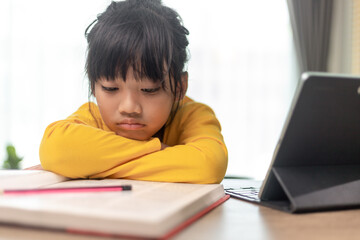 Little Asian girl sitting alone and looking out with a bored face, Preschool child laying head down on the table with sad  bored with homework, spoiled child
