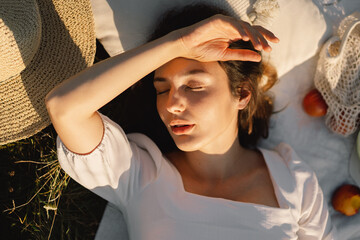 Beautiful romantic young woman lying on a blanket on a summer meadow. Time for yourself. Relaxing on summer meadow. A girl with beautiful hair is enjoying the summer weather.