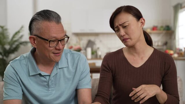caring Asian daughter consoling her frustrated retired father and patting her back in the living room at home. the depressed old man cries and buries his face in his hands while listening