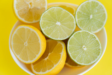 Fototapeta na wymiar Top view of fresh lemons and limes in bowl on yellow background