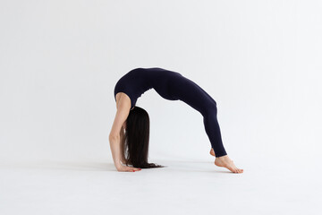 a beautiful young girl with dark hair stands in the Urdhva Dhanurasana pose on a white background. Yoga class