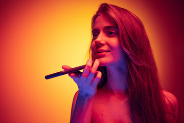 Obraz premium Portrait of young girl recording voice message on phone isolated over gradient red yellow background in neon light
