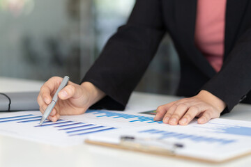 Business woman holding pen pointing at financial report chart document, It is analyzing marketing data to plan the company's finances and growth.