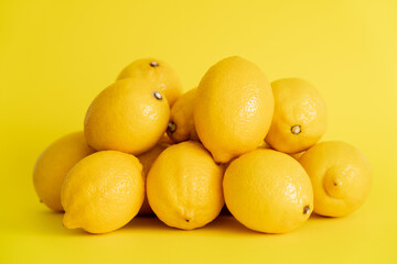 Heap of fresh lemons on yellow surface