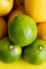 Close up view of fresh green limes near blurred lemons on yellow surface