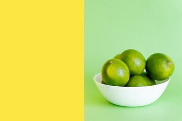 Ripe limes in bowl on green and yellow background