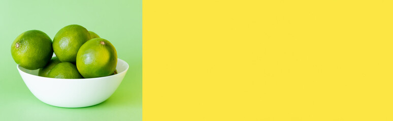 Fresh limes in bowl on green and yellow background with copy space, banner