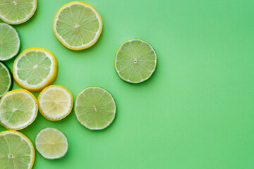 Top view of sliced fresh lemons and limes on green background with copy space