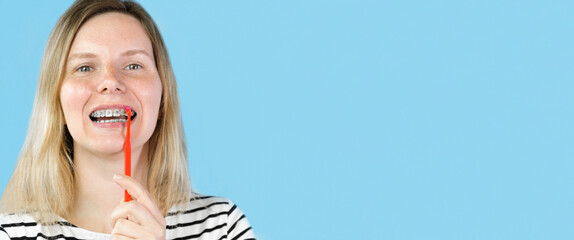Young woman with dental braces brushing teeth isolated on blue colour background. Studio. Cute...