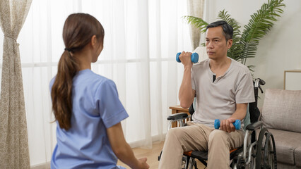 backside of asian female physiotherapy resident care attendant helping older male wheelchair user do rehab exercise with dumbbells at home. she shows him how to do with gestures