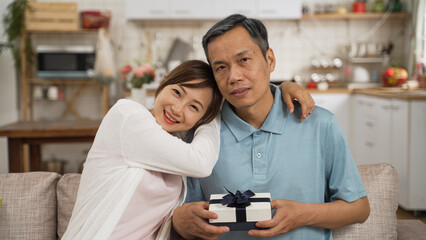 portrait of asian retired father and adult daughter looking at camera with Father’s Day gift in...