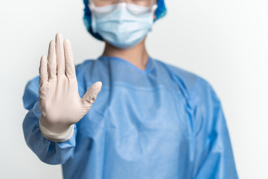 Doctor or nurse wearing protective suit and mask showing stop gesture on the white background.