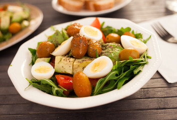 fresh salad of arugula, avocado, cherry tomatoes with olives and quail eggs in white bowl