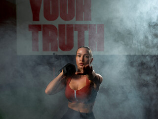 Determined young sportswoman doing lunges with dumbbell in gym