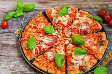 Close up of   classic  Italian Pizza   with Ham and salami . Fresh basil,tomato sauce ,mozzarella cheese , mushrooms and  green peppers
