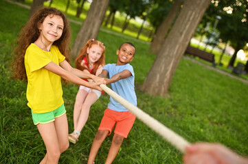 group of preschool children - boys and girls compete in a tug of war against the background of a park and greenery.
