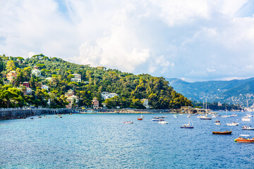 Fototapeta premium Fishing boats moored on water in harbor of Ligurian and Mediterranean Sea near coastline of Riviera di Levante of National park Cinque Terre Coast with blue sky, Riomaggiore village, Liguria, Italy.