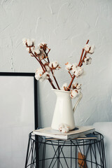 On the coffee table there is a white vase with dry cotton branches.
