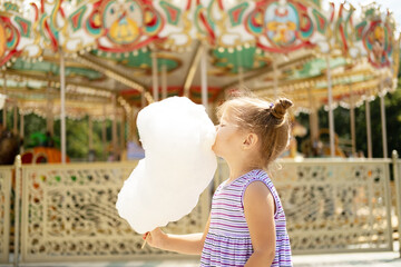 Funny blonde girl in colorful dress eating cotton candy at the carnival