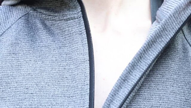 A woman's hand fastens and unzips a gray jacket on the street, put on a jacket, fasten the lock on clothes